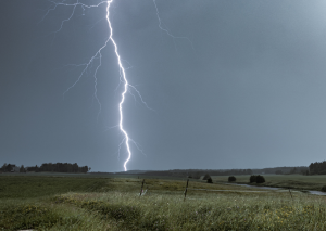 ein Feld au dem ein Blitz einschlägt, der Himmel ist mit dunklen Wolken bedeckt