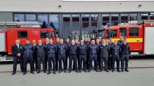 Brandmeisteranwärter stehen auf dem Hof des Gefahrenabwehrzentrums, hinter ihnen stehen zwei Feuerwehrautos