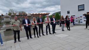 Mehrere Personen schneiden ein Band vor einem Platzmit Brunnen durch