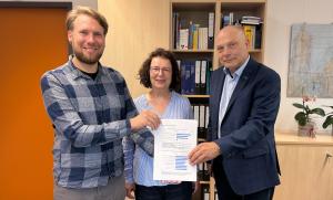 Drei Menschen halten ein Dokument in die Kamera