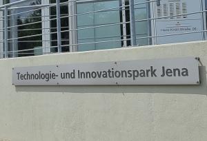 Blick ein Schild vor einem Gebäude mit der Aufschrift "Technologie- und Innovationspark Jena".