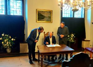 Olaf Scholz trägt sich ins Goldene Buch der Stadt Jena ein. Er sitzt am Tisch. Oberbürgermeister Dr. Thomas Nitzsche und Bürgermeister Christian Gerlitz stehen neben ihm.