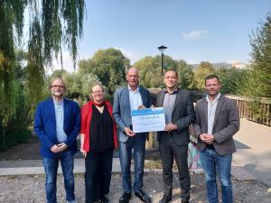 Fünf Personen stehen an der Griesbrücke in Jena. Ein Scheck wird von zwei Personen in der Hand gehalten