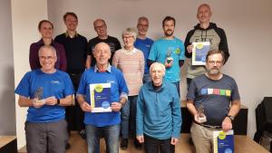 Elf Männer und Frauen stehen auf zwei Stufen hintereinander und blicken in die Kamer.