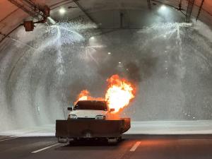 Ein Auto steht im Tunnel und brennt. Die Brandbekämpungsanlage versprüht Löschschaum.