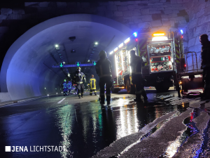 Vor dem Jagdbergtunnel steht ein Feuerwehrauto. Feuerwehrleute laufen im Tunnel. Das Blaulicht spiegelt sich in ausgelaufenem Wasser.