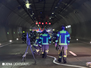 Feuerwehrleute laufen durch den Tunnel. Löschschläuche liegen auf dem Boden.
