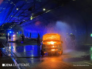 Ein Auto brennt im Tunnel. Feuerwehrleute löschen es.