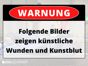 Über einem Bild liegt ein Warnhinweis mit der Aufschrift: Warnung: Folgende Bilder zeigen künstliche Wunden und Kunstblut.