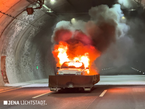 Im Tunnel brennt ein Auto. Es steht in einer Metallwanne, die auf Paletten steht, um den Asphalt zu schützen. 