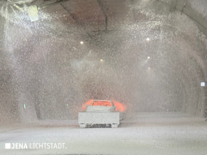 Die stationäre Brandbekämpfungsanlage sprüht von der Decke Schaum auf das brennende Auto. Der Boden ist von Löschschaum bedeckt.