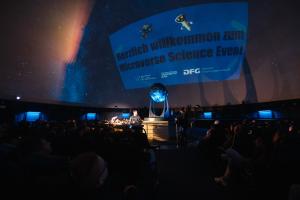 Im Zeiss-Planetarium wird ein Textbild an den Himmel projeziert, Menschen schauen dabei zu.