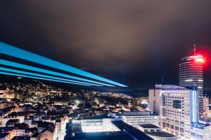 Das Foto zeigt Jena im Dunkeln mit erleuchteten Gebäuden und einem großen Laserstrahl am Himmel.
