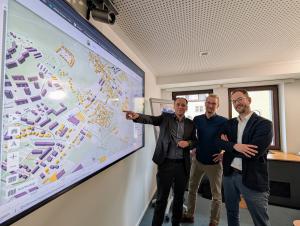 Christian Gerlitz, Bürgermeister und Dezernent für Stadtentwicklung und Umwelt der Stadt Jena, Kevin Muschalle-Momberg Klimaschutzkoordinator der Stadt Jena, und Christian Dornack, Bereichsleiter Strategie bei den Stadtwerken Jena Netze stehen vor einer Karte der Kommunalen Wärmeplanung.