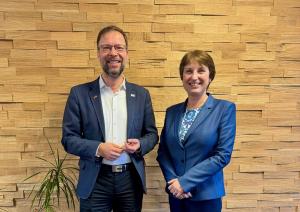 Oberbürgermeister Thomas Nitzsche und Botschafterin Adriana Stănescu stehen in seinem Büro nebeneinander und schauen in die Kamera.