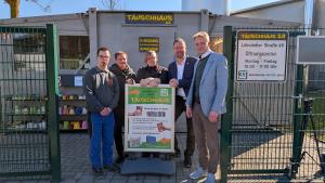 Vor dem Tauschhaus 2.0 stehen 5 Personen um ein Aufsteller, der Hinweise zu Gegenständen im Tauschhaus gibt.