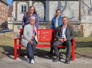 Vier Menschen sitzen auf einer roten Bank. 