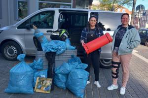 Vor einem grauen Kastenwagen stehen zwei Frauen neben diversen Tüten und KIsten, in denen sich Spenden befinden.