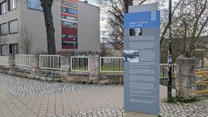 Eine Stele mit Informationen zu Robert J. Büchler und dem Todesmarsch am 11. April 1945 steht auf einem Gehweg. Im Hintergrund ist ein Schulgebäude zu sehen.