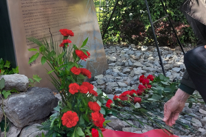 Hand, die rote Rose vor Gedenkstele ablegt