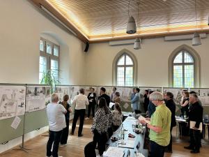 Sitzung einer Jury: mehrere Personen schauen sich Entwürfe an, die an Pinnwänden befestigt sind.