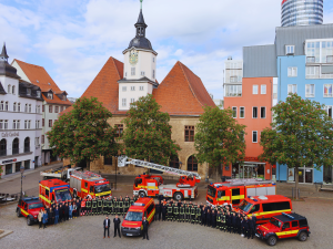 Viele Feuerwehrleute und Fahrzeuge stehen vor dem Jenaer Rathaus und schauen in die Kamera.