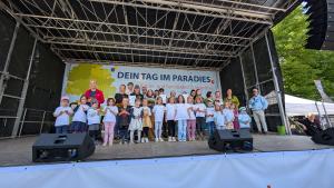 Auf einer Bühne stehen eine Reihe von Kindern und Jugendliche plus einige Erwachsene.