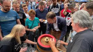 Ein Mann sticht ein Bierfass an, viele Menschen beobachten ihn