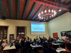 Menschen sitzen an Tischen in einem historischen Gebäude, im Vordergrund steht ein Mann an einem Rednerpult