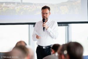 Ein Mann steht vor einem Publikum und spricht in ein Mikrofon.