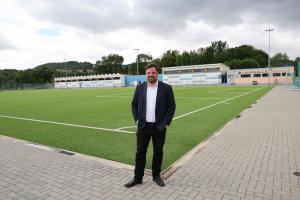 Ein Mann im Anzug steht am Rand eines Fußballplatzes.