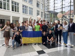 Einen Gruppe von Jugendlichen steht mit ein paar erwachsenen für ein Gruppenfoto zusammen und halten eine Ukraine-Flagge.