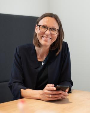 Foto von Stefanie Braune, die mit einem Handy in der Hand an einem Tisch sitzt