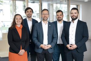 Eine Frau und vier Männer stehen nebeneinander in einem Innenraum.