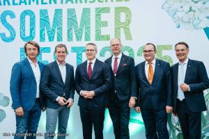 Sechs Männer in Anzügen stehen nebeneinander und lächeln in die Kamera.