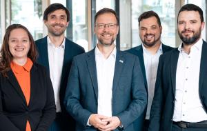 Eine Frau links und 4 Männer stehen lächelnd nebeneinander.