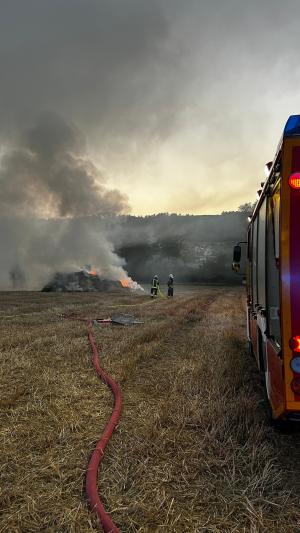 Feuerwehrauto auf einem Feld mit starkem Rauch und brennenden Strohballen