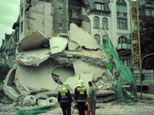 Drei Menschen schauen auf ein eingestürztes Gebäude.