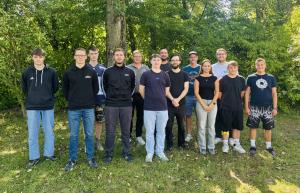 14 Personen stehen für ein Gruppenbild in zwei Reihen neben- bzs. hintereinander