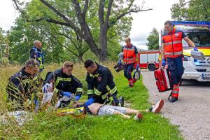 Feuerwehr und Notarztteam eilen zu einer still liegenden Person am Boden.