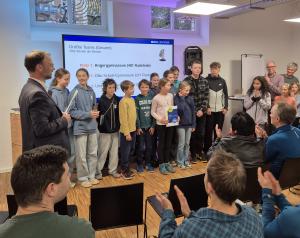 Der Oberbürgermeister steht mit einer Gruppe vor Schülern vor Publikum. Eine Schülerin hält eine Urkunde, eine andere einen Pokal.