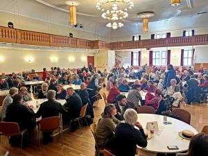 Menschen sitzen an Runden Tischen in einem großen Saal