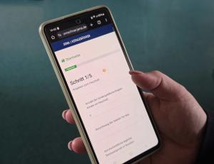 Eine Hand hält ein Smartphone auf dem der Kitagebührenrechner der Stadt Jena geöffnet ist.