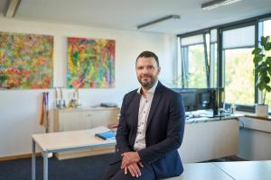 Mann sitzt auf einem Tisch in einem Innenraum und lächelt