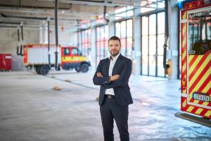 Mann in blauem Anzug steht in einer Halle mit Feuerwehrfahrzeugen