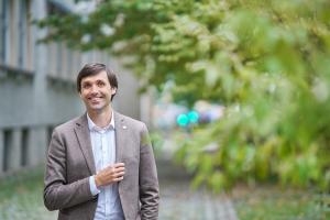 Mann in braunem Anzug steht im Außenbereich und lächelt