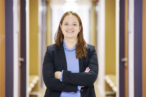 Frau steht mit verschränkten Armen in einem Korridor und lächelt in die Kamera