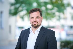 Mann in blauem Anzug steht im Außenbereich und lächelt