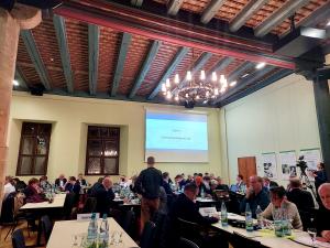 Stadtratsmitglieder sitzen an Tischen im historischen Rathaus, ein Redner steht am Mikrofon