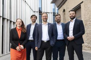 Eine Frau und vier Männer vor zwei Gebäuden